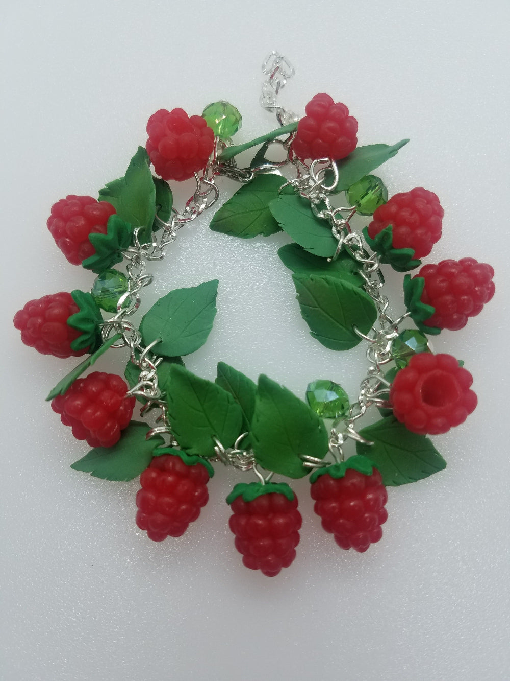 Handmade polymer clay raspberry charm bracelet arranged in a circle with green leaves and sparkling crystals