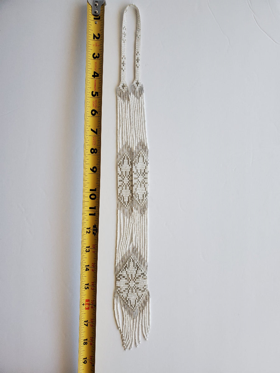 White and silver beaded gerdan necklace laid flat beside a tape measure showing its length